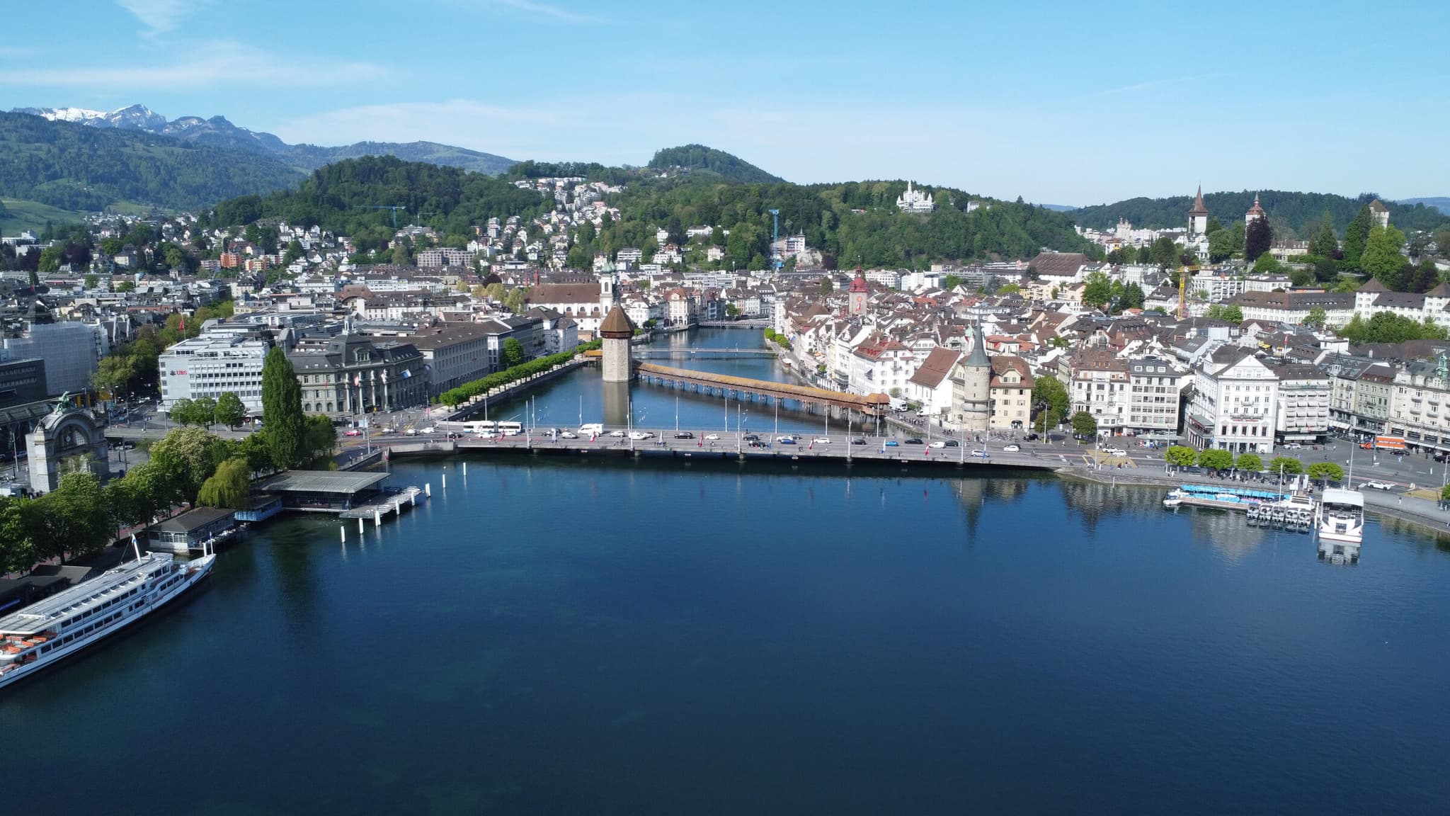 Veduta aerea di Lucerna con il Ponte della Cappella e la torre d'acqua, il centro storico lungo la Reuss, il Lago dei Quattro Cantoni e le montagne innevate.