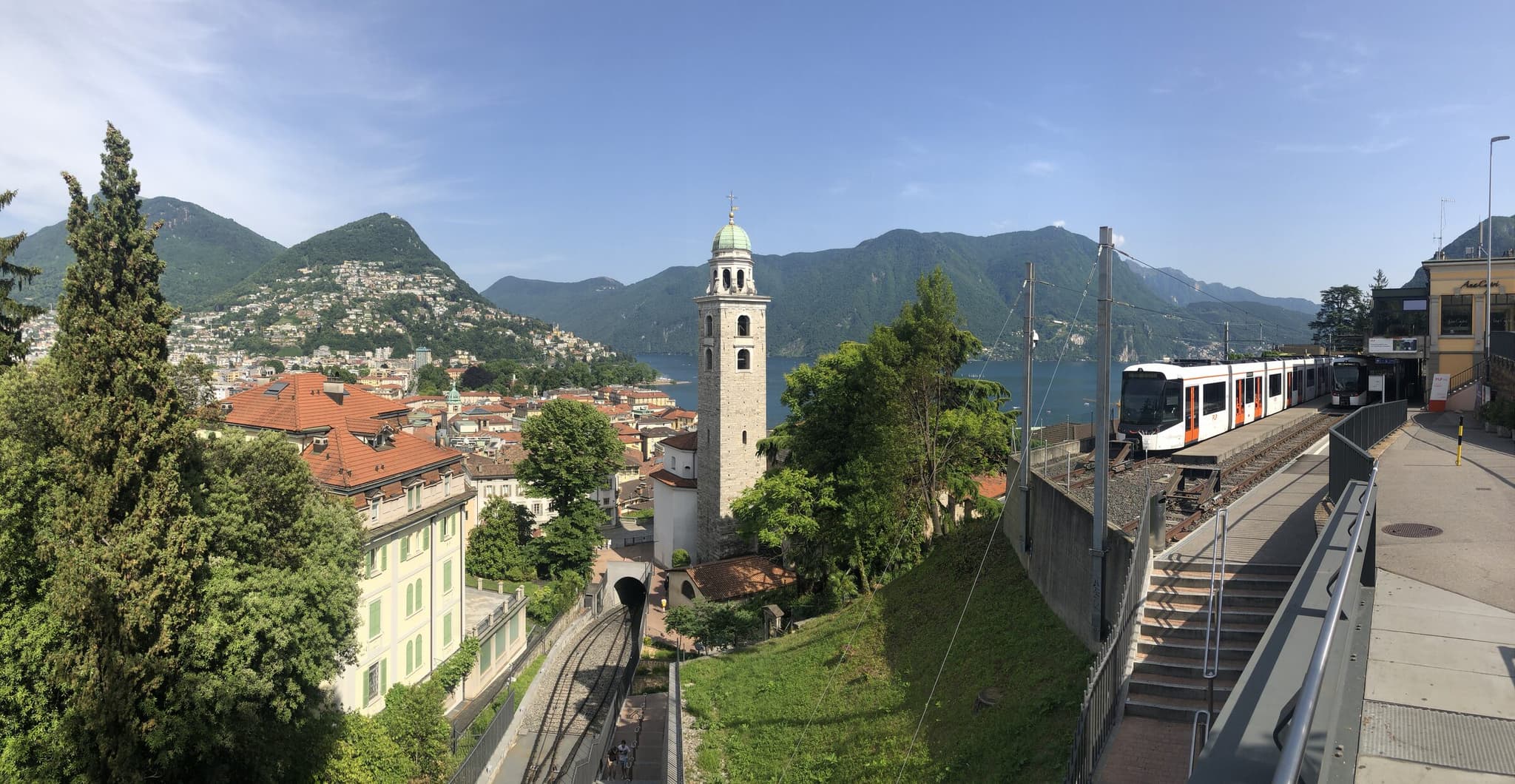 Vue sur la ville de Lugano avec le clocher de la cathédrale San Lorenzo, le lac de Lugano, les montagnes et le funiculaire menant à la gare.
